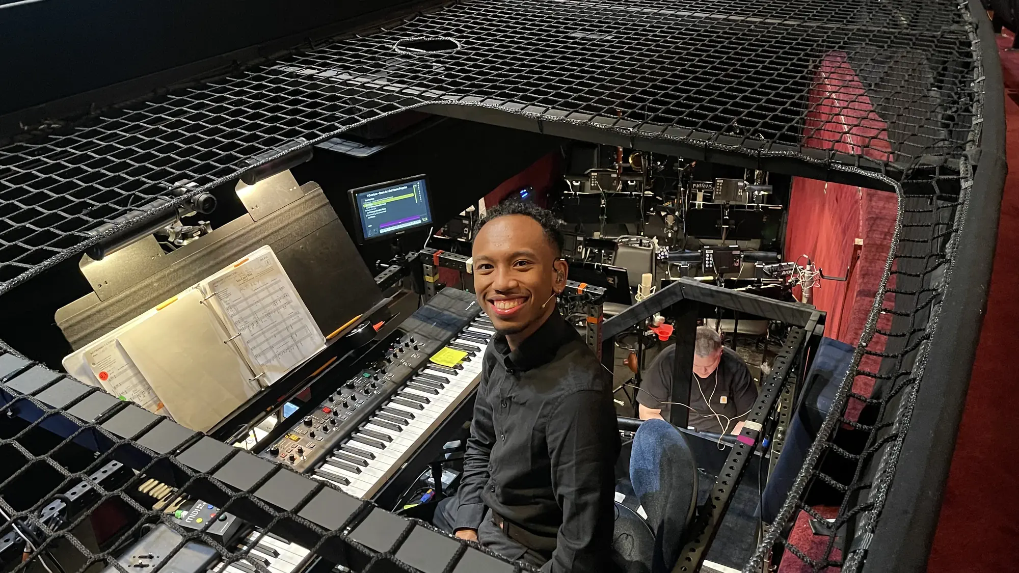 Patrick B. Phillips smiling from a theater orchestra pit at a keyboard setup